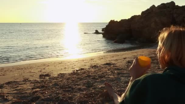 여자는 해변에 일출을 존경합니다 소녀는 카메라로 그녀와 앉아있다 고품질 — 비디오
