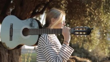 Parkta burnunda piercingle dolaşan, omzunda siyah bir gitarla gezen hafif görünümlü bir hipster kız. Video bir gencin etrafında çekildi. Yüksek kaliteli FullHD görüntüler