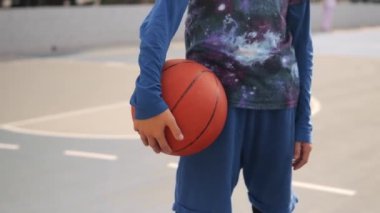Bir çocuk basketbol sahasında duruyor ve topa yakın çekim yapıyor. Elinde top ve basketbol sepetiyle ayakta duran bir gencin sinematik çekimi. Yüksek kaliteli FullHD görüntüler