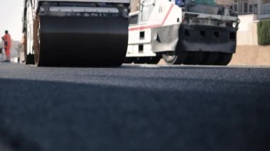 Güneşe yeni bırakılmış bir asfalt tabakası. Yol yüzeyi tamiri. Yeni bir yol inşaatı. Patenler asfaltı düzleştirip sıkıştırıyor. Yol silindirleri. Güneş parlıyor. Yüksek kaliteli FullHD görüntüler