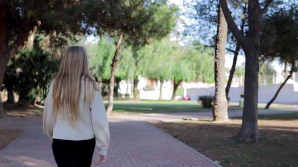 Dziewczyna Blond Włosami Białym Swetrze Czarnymi Dżinsami Spaceruje Alejką Parku — Wideo stockowe