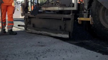 Asfalt kaldırım taşı taze sıcak asfalt karışımını yakın çekim yapar. Yakınlarda bir işçi işi yakından izler. Yüksek kaliteli FullHD görüntüler