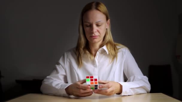 셔츠에 소녀는 어두운 뒤에서 Rubiks 큐브를 테이블에 앉아있다 고품질 — 비디오
