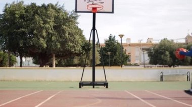 Çocuk oyun parkında basketbol oynuyor, gün batımında sepetin içine atıyor kameranın önünde basket oynuyor, yerleşim bölgesinde basketbol oynuyor. Yüksek kaliteli FullHD görüntüler
