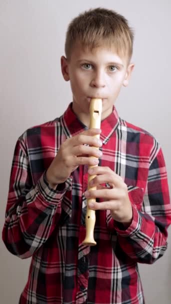 一个穿着格子红衬衫的少年演奏长笛 一个在房间里吹奏长笛的男孩的肖像 优质Fullhd影片 — 图库视频影像