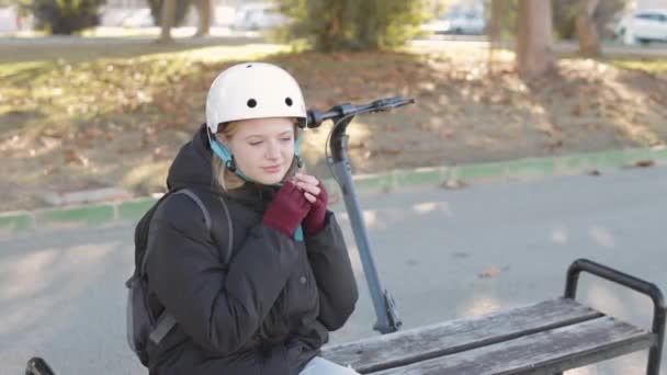 Девушка Подросток Пиджаке Снимает Белый Шлем Сидя Скамейке Парке Рядом — стоковое видео