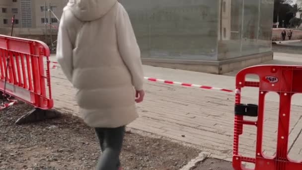 一个穿着轻便夹克和牛仔裤的女孩走在带子下面 城市街道上有红白相间的保护带 街道维修 高质量的4K镜头 — 图库视频影像