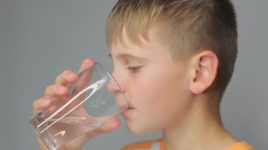 Avrupalı görünümlü tatlı çocuk gri arka plandaki cam bardaktan su içiyor. Yüksek kaliteli FullHD görüntüler