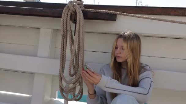 10代の少女は 青い海の背景に彼女の携帯電話のビデオを見ている船に乗っている 高品質の4K映像 — ストック動画