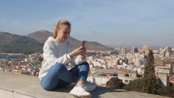 白いスウェットシャツの女の子は 街の背景に立って ビデオ接続を介して話します 高品質の4K映像 — ストック動画