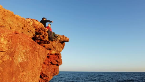 パパと息子は岩の上に座って海を見ている 父と息子は崖の端に座っている 観光客は岩でリラックスして海を楽しむ 高品質の4K映像 — ストック動画