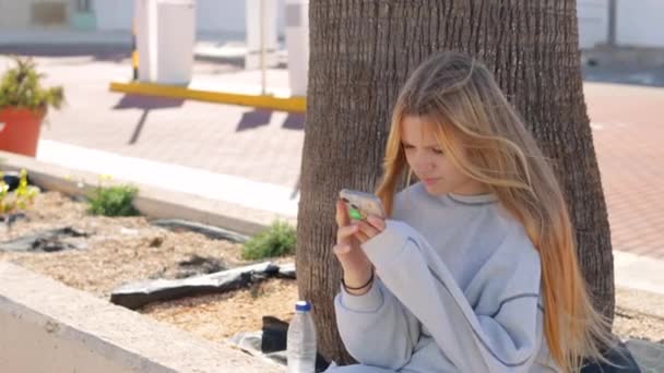 一个少女坐在公园里 手里拿着电话 一个青少年把他的手指放在手机屏幕上 多样性的概念 优质Fullhd影片 — 图库视频影像