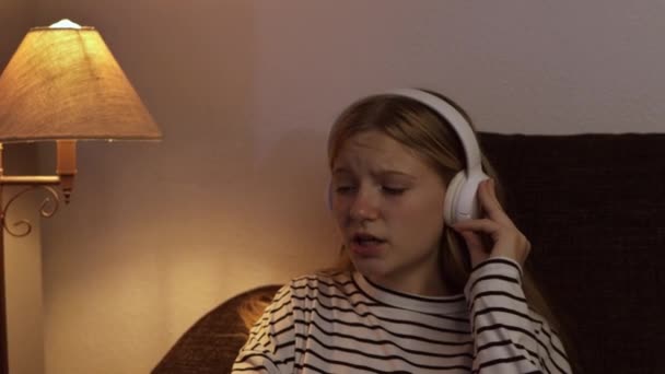 Çizgili Kazaklı Genç Bir Kız Kanepede Oturmuş Kulaklıkla Müzik Dinliyor — Stok video