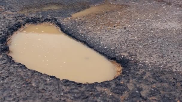 在乡间一条摇摇欲坠的道路中间的一个大坑洞 雨中道路上的一个小孔的闭合 优质Fullhd影片 — 图库视频影像