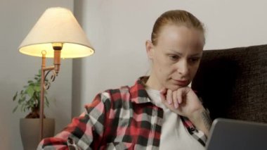 Kanepede rahat bir şekilde oturan, açık tenli bir kız bilgisayarında özenle çalışıyor, parmaklarını klavyede hızla hareket ettiriyor ve görevine konsantre oluyor. Yüksek kalite FullHD