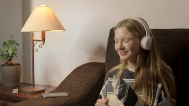 リビングルームでは 鼻ピアスを持つヒップスターの少女がソファに座り ヘッドフォンを通して彼女の音楽に吸収され 彼女のユニークなスタイルと雰囲気を示しています 高品質のフルHd映像 — ストック動画