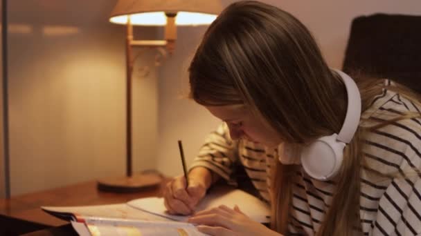 自宅で勉強しているヘッドフォンを着ている十代の少女 十代の子供たちに宿題を教える 高品質の4K映像 — ストック動画