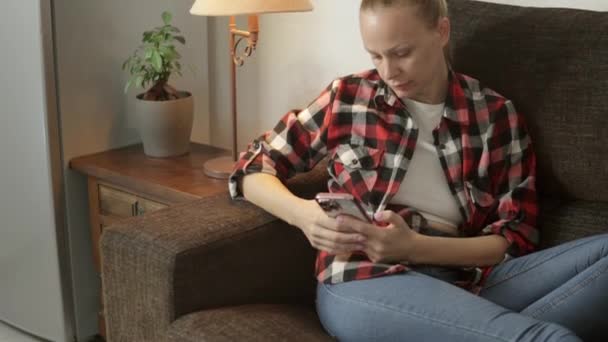 Dziewczyna Codziennych Ubraniach Siedzi Kanapie Telefonem Ręku Jej Wyraz Twarzy — Wideo stockowe