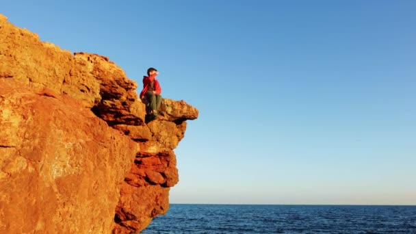 Ένας Έφηβος Πορτοκαλί Μπουφάν Κάθεται Στα Βράχια Και Κοιτάζει Θάλασσα — Αρχείο Βίντεο