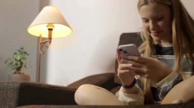 Oturma odasının sıcacık atmosferinde, burnu piercingli hippi bir kız rahatça oturur, elleri telefonla meşguldür. Kamera açısı, düşük perspektiften benzersiz bir bakış açısı sunuyor. Yüksek