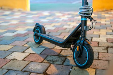 Parktaki kaldırımda duran elektrikli scooter 'ın tekerleklerine yakın plan, modern kentsel hareketlilik ve çevre dostu ulaşım.