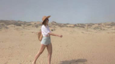 Bir yaz günü çölde yürüyen kız, beyaz tişörtlü, hasır şapkalı ve şortlu bir kız...