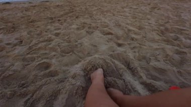 Kız sahilde oturmuş, denize hayran, bronzlaşmış bir kızın bacaklarına yakından bakıyor, deniz ve dramatik bir gökyüzü. Yüksek kaliteli FullHD görüntüler