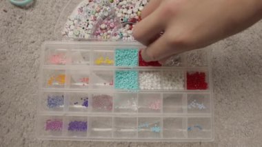 Bir sürü renkli boncuklarla dolu plastik bir kavanozu tutan el.