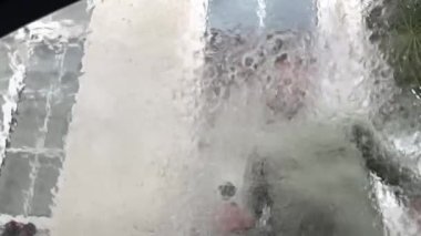 Adam basınçlı jetle otomobilin ön camını yıkıyor. El yıkama servisinde akan suyla birlikte bulanık cam. İçeriden yakın görüntü. Yüksek kaliteli FullHD görüntüler