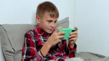 Genç bir çocuk telefonunu kanepede yatarak geçirir. İnternet, mobil uygulamalar, boş zamanlardaki gençler, çevrimiçi mesajlar. Yüksek kalite 4k görüntü