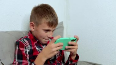 Genç bir çocuk telefonunu kanepede yatarak geçirir. İnternet, mobil uygulamalar, boş zamanlardaki gençler, çevrimiçi mesajlar. Yüksek kalite 4k görüntü