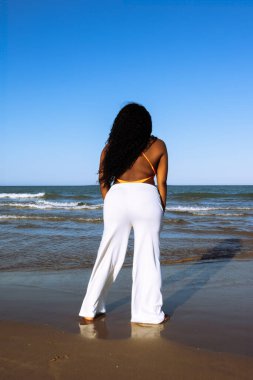 Kıvırcık gülümseyen Afro-Amerikan esmer tenli kadın deniz üzerinde yürüyor. Hafta sonu gökyüzü ufkuna karşı ırklar arası kadınlar. Karışık ırk insanları, etnik köken, çeşitlilik.