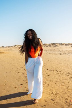 Tropikal plajda bikinili güzel Afrikalı Amerikalı kadın. Denizde gülümseyen esmer kadın portresi. Mayolu esmer kız sahilde yürüyor ve eğleniyor..