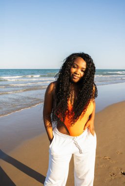 Tropikal plajda bikinili güzel Afrikalı Amerikalı kadın. Denizde gülümseyen esmer kadın portresi. Mayolu esmer kız sahilde yürüyor ve eğleniyor..