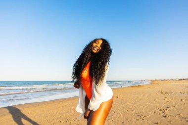 Kıvırcık gülümseyen Afro-Amerikan esmer tenli kadın deniz üzerinde yürüyor. Hafta sonu gökyüzü ufkuna karşı ırklar arası kadınlar. Karışık ırk insanları, etnik köken, çeşitlilik.