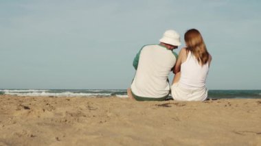 Deniz kıyısındaki genç çift. Genç adam ve kadın gün batımında sahilde dinleniyorlar..