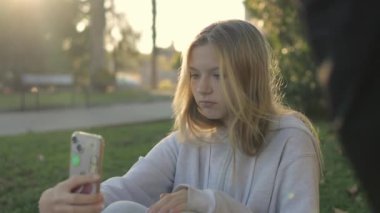 Güzel görünümlü genç bir kız parkta çimlerin üzerinde otururken selfie çeker. Yüksek kaliteli FullHD görüntüler