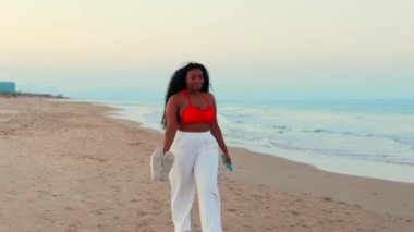 Gün batımında sahilde yürüyen bir kadın. Yaz tatili. Güzel Afrikalı Amerikalı kadın.
