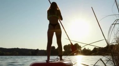 Gün batımında gölde kürek çeken genç bir kadın.