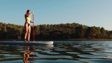 # Kız güneşli bir yaz gününde göl kenarındaki kürek tahtasının üzerinde zıplıyor #