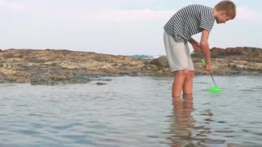 Genç bir çocuk, elinde topla denizde olta atıyor.