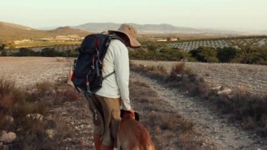 Sırt çantalı bir yürüyüşçü ve ufukta dağlarda yürüyen bir köpek.