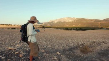 Sırt çantalı bir adam dağın tepesinde ve uzaktan kumandalı bir sırt çantası var.