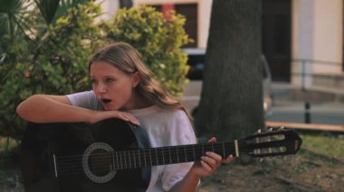 Genç kız parkta gitar çalıyor.