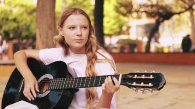 Beyaz tişörtlü güzel kız akustik gitarla oynuyor..