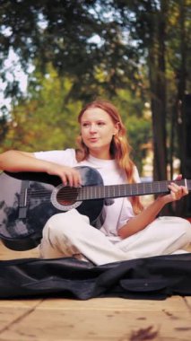 Kız sonbahar parkında gitar çalıyor.