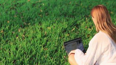 Baharda çimlerin üzerinde dizüstü bilgisayarı olan güzel bir kız.