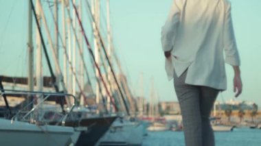 Beyaz gömlekli ve kot pantolonlu bir kadın gün batımında deniz limanında yürüyor..