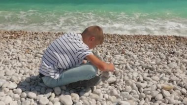Çocuk taşlara oturur ve denize bakar.