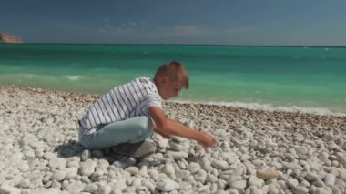Adam denizin kenarında oturur ve kameraya bakar, adam taşların üzerine oturur..
